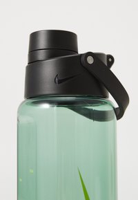 Nike waterfles met een doorzichtig teal lichaam, een zwarte schroefdop en een stevige handgreep. Voorzien van maataanduidingen aan de zijkant.
