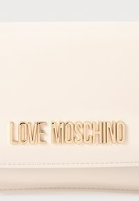 Bleda roza umetna usnjena denarnica z zlatim metalnim logotipom "LOVE MOSCHINO", gladka tekstura in našitki ob robu.