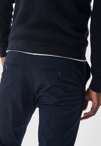 Granatowy sweter o teksturowanym splotcie, w połączeniu z ciemnoniebieskimi spodniami z dwiema tylnymi kieszeniami zapinanymi na guziki. Prosty i funkcjonalny design.