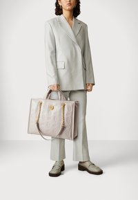 Sac fourre-tout en cuir gris clair avec un logo estampé, des accents de chaîne dorée et des poignées doubles ; associé à un costume gris clair assorti et des chaussures.