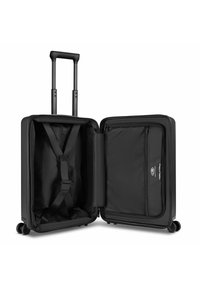 Maleta negra de carcasa dura con asa extensible, cuatro ruedas, compartimentos abiertos que muestran correas cruzadas en un lado y un bolsillo de malla con cremallera en el otro.