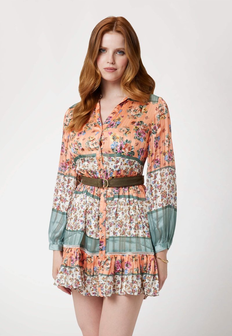 Gėlėta suknelė su oranžine ir žalia spalvų palete, mygtukų užsegimu priekyje, raukšlėtu apdailu ir susiaurinta juosmeniu su diržo detale.