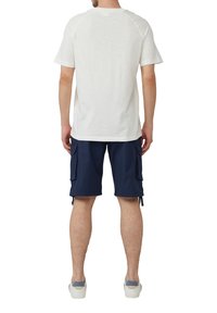 Weißes Kurzarm-T-Shirt mit Rundhalsausschnitt, kombiniert mit marineblauen Cargo-Shorts mit Seitentaschen und verstellbaren Kordeln. Weiße Sneakers.