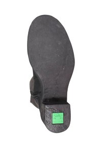 Suela de zapato negra con una superficie de goma texturizada, que presenta un logo de rana verde en el talón y una curva ascendente en la zona de los dedos.