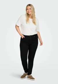 Crne uske traperice s glatkom teksturom i dizajnom od pet džepova, uparene s bijelim majicom kratkih rukava koja ima čipkastu obrub i smeškim tenisicama.