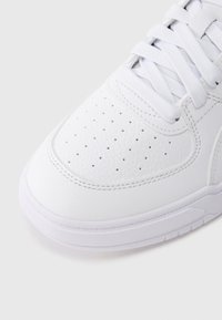 Λευκό αθλητικό παπούτσι με υφή από δέρμα στο πάνω μέρος, διάτρητο μπροστινό μέρος για αερισμό και επίπεδα λευκά κορδόνια. Λείο λευκό ελαστικό πάτο.