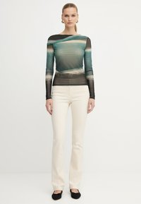 Top a maniche lunghe, adeso in turchese trasparente e nero con un motivo a tema acquatico. Abbinato a pantaloni a campana color crema e ballerine nere.