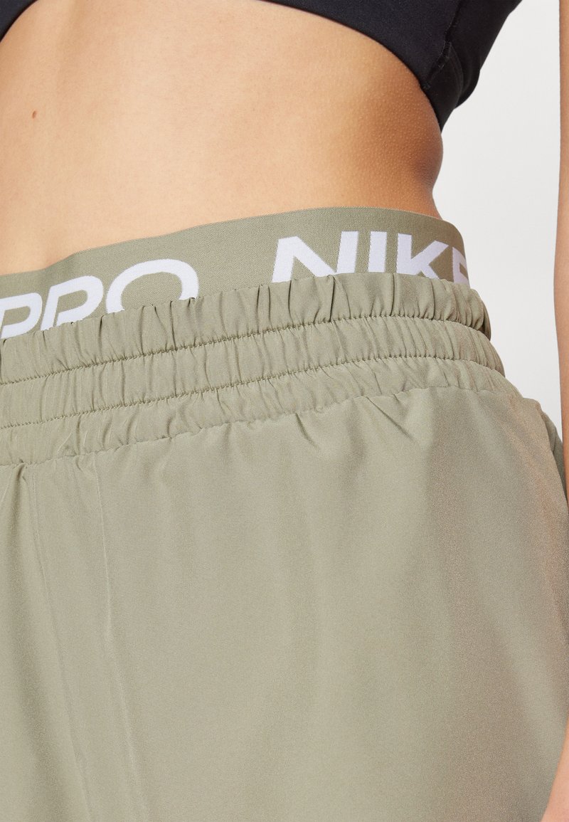 Cintura ajustable Nike Pro en verde oliva claro, con logo blanco. Tejido suave y liso con textura fruncida, cortado justo por encima de la cintura.