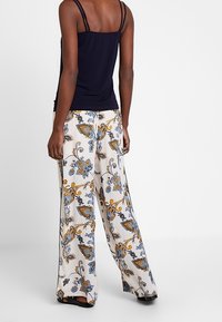 Top nero a spalline con pantaloni larghi che presentano un motivo floreale e paisley in blu, oro e nero su uno sfondo chiaro.