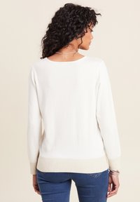 Maglione color crema con collo rotondo, maniche lunghe e orlo inferiore texture. Indossato con jeans blu. Materiale morbido e vestibilità rilassata.