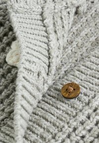 Tissu tricoté gris avec des motifs texturés ; comporte un bouton marron portant l'inscription "SUIVANT" et un accent crème. Design chaud, doux et volumineux.