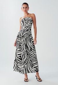 Axelbandslös svartvit klänning med zebramönster, med åtsittande byst och flödande kjol, gjord av lätt tyg.
