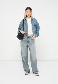 Denimska jakna v svetlo modri, širok kroj; bela kratka majica; zbledeli modri naravnost krojeni kavbojke; črna torbica za čez ramo; črno-bele superge.