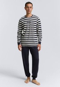 Cămașă cu mânecă lungă cu dungi în albastru închis și crem, cu guler rotund și logo, asortată cu pantaloni uni albastru închis, ambele realizate dintr-un material moale.