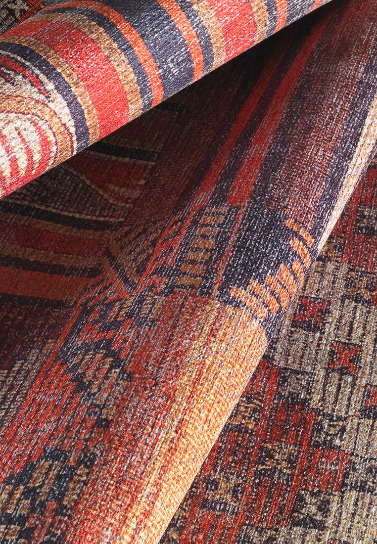Dywan tekstylny z pomarańczowymi, czerwonymi i granatowymi wzorami oraz geometrycznymi i plemiennymi motywami. Teksturowana powierzchnia z detalami wplecionego wzoru.