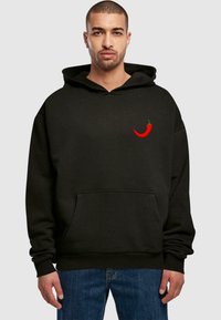 Czarna, oversize bluza z kapturem z wyszywaną czerwoną papryczką chili na piersi, z kieszenią z przodu oraz ściągaczami przy mankietach i u dołu.