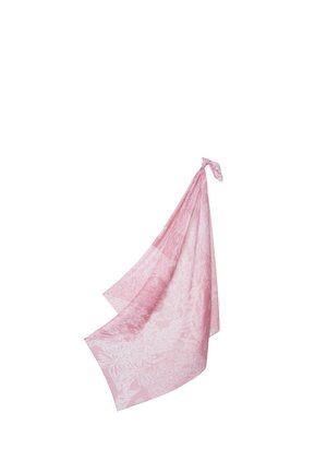 Foulard en soie rose clair avec des motifs floraux blancs, noué lâchement à un coin, flottant doucement sur un fond blanc.