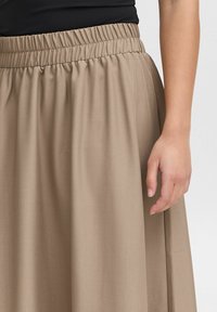 Khaki elastic waist skirt with a smooth, flowing fabric. Features gentle pleats and a relaxed fit, paired with a fitted black top.