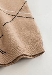 Gros plan d’un tissu tricoté beige avec un ourlet côtelé et des motifs abstraits en lignes noires et blanches.