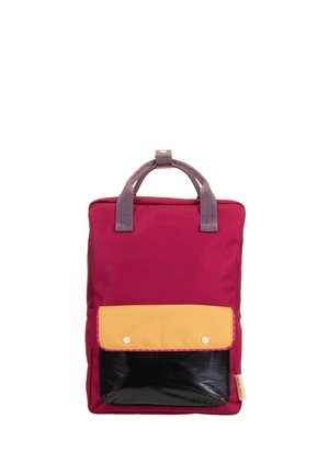 Sac à dos rectangulaire rouge avec poignées violettes et poche avant avec rabat jaune et base noire, sur fond blanc.