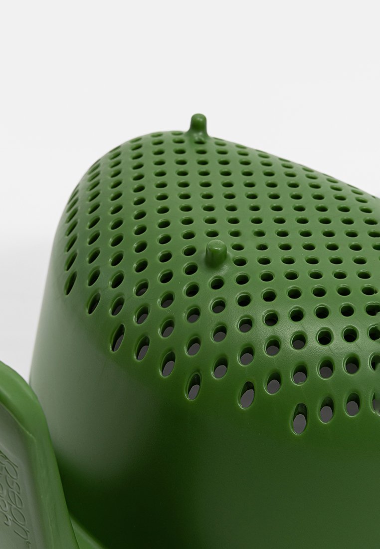Objeto de plástico verde con una superficie perforada, forma redondeada y dos puntos salientes en la parte superior, que presenta una textura suave y bordes curvados.