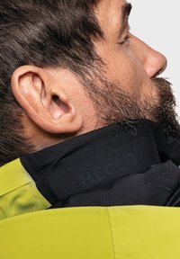 Collare nero con marchio RECCO accanto a un tessuto giallo brillante, caratterizzato da una consistenza liscia e una vestibilità aderente attorno al collo.