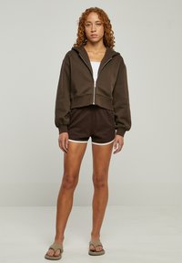 Brunet avkortet hettegenser med glidelås, kombinert med brune shorts med hvite detaljer. Glatt stoff og avslappet passform.