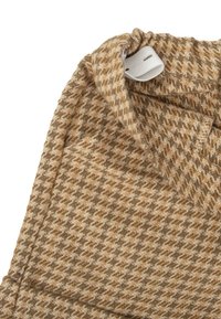 Tejido de pata de gallo marrón y beige con una textura suave, que cuenta con una cinturilla elástica fruncida y una etiqueta blanca.