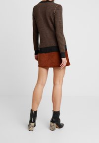 Pull rayé noir et marron avec texture en maille côtelée ; associé à une jupe en velours côtelé couleur rouille et des bottines noires avec talons imprimés serpent.