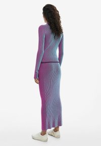 Lang gestreiftes Strickkleid in einem Farbverlauf von Pink und Blau. Figurbetonte Silhouette mit langen Ärmeln, kombiniert mit weißen Freizeitschuhen.