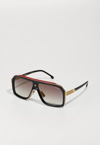 Occhiali da sole neri con dettagli in oro, lenti sfumate e rifiniture rosse sulla parte superiore. Bracci eleganti con marchio in rilievo.