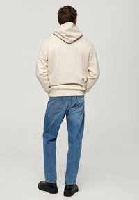 Beige hoodie met een trekkoord, gecombineerd met lichtblauwe recht gesneden jeans en zwarte, dikke laarzen. Eenvoudige en casual outfit.