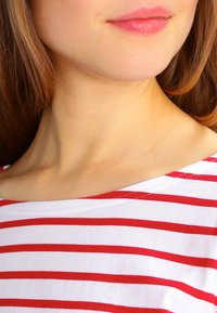 Camicia bianca con strisce orizzontali rosse, scollatura rotonda, tessuto morbido, inquadratura ravvicinata che enfatizza colore e texture.