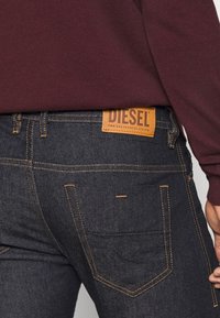 Mörk denimjeans med orange sömmar, med en läderlogotyp som är märkta "DIESEL" på baklinningen och standard bakfickor.