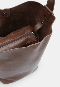 Brun læder tote bag med en tekstureret overflade, der har en intern lynlåspose, cirkulær bund og en rummelig åben top.