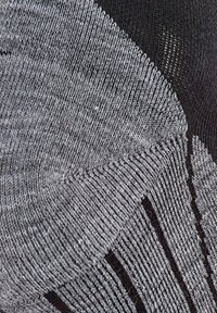 Tissu tricoté gris avec un mélange de tons clairs et foncés. Présente des sections texturées et un design côtelé avec des accents noirs contrastants.