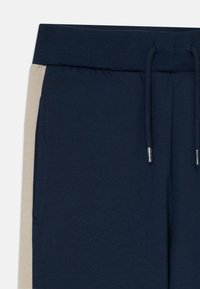 Pantalons de survêtement bleu marine avec des panneaux latéraux beiges, une taille élastique côtelée et des cordons de serrage bleu marine avec des embouts en métal.