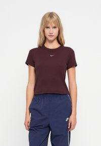 Bordo trumpų rankovių prigludusi marškinėlių su griovelių tekstūra ir maža balta Nike logo ant krūtinės, derinami su tamsiai mėlynomis šoninėmis juostelėmis kelnių.