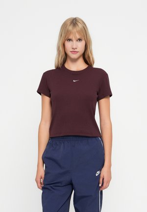 T-paita, jossa on lyhyet hihat ja tiukka istuvuus, väriltään punaharmaa, jossa on kankaan röpelöinen tekstuuri ja pieni valkoinen Nike-logo rinnassa, yhdistettynä tummansinisiin narutaskuhousuihin.
