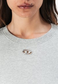 Light gray sweatshirt with a round neckline, featuring a small silver logo patch at the collar and a soft, textured fabric.