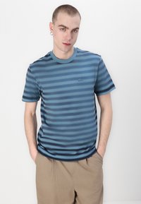 Pasiasty T-shirt w odcieniach niebieskiego z okrągłym dekoltem, krótkimi rękawami i małym logo na piersi. Wykonana z gładkiego materiału o miękkiej teksturze.