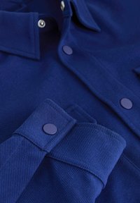 Marineblaues Hemd aus strukturiertem Stoff, mit durchgehender Knopfleiste und passenden Knöpfen sowie mit einem strukturierten Kragen und Manschettendetails.