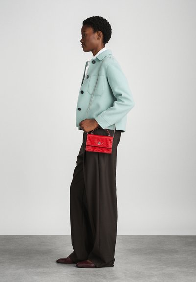 Red crocodile-embossed handbag with a chain strap, paired with a mint green jacket and brown wide-leg trousers, worn with maroon shoes.