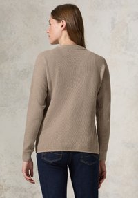 Maglione in maglia testurizzata beige con collo rotondo, maniche lunghe e vestibilità comoda, abbinato a jeans blu scuro. Modello rivolto di spalle alla fotocamera.