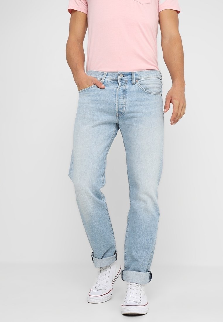 Vaqueros de mezclilla azul claro con un corte relajado, con puños enrollados, diseño de cinco bolsillos y un ligero desgaste. Combinados con una camiseta rosa y zapatillas blancas.