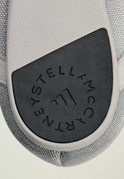 Gros plan sur la semelle d'une basket montrant une section de grip circulaire noire avec le logo Adidas et le texte « Stella McCartney » autour.