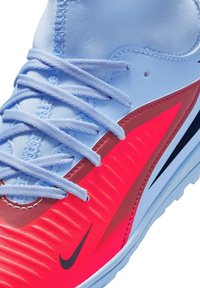Nike atletiksko med en blå overdel, røde accenter og tekstureret design. Har flade blå snørebånd og en kontrasterende sort logo.