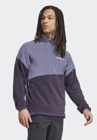 Lilla fleece-pullover med halv-zip krave, der har farveblokering design og et lille logo. Blød tekstur og afslappet pasform.