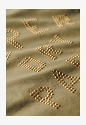 Olivengrønt stof med hævede guldstifter, der danner bogstaver og former, hvilket skaber et struktureret mønster over overfladen.