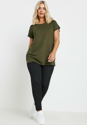 Olijfgroene t-shirt met korte mouwen, relaxte pasvorm, ronde halslijn. Gecombineerd met zwarte slim-fit broek en witte sneakers.